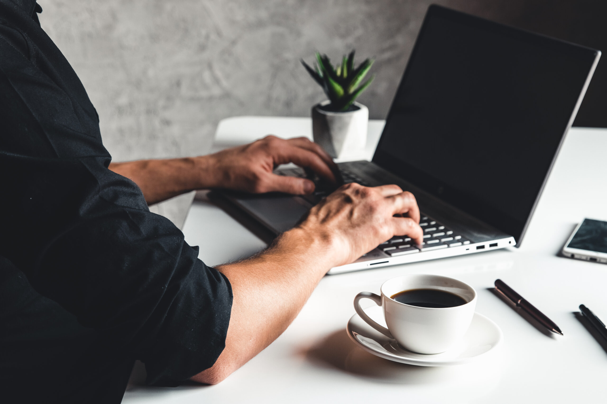 A man types on a laptop, business concept, glasses, a cup of coffee and a pen on a gray background